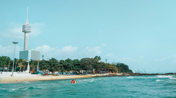 Scenic view of Dongtan Beach in Pattaya with the Pattaya Park Tower in the background, featuring turquoise waters, palm trees, and beachgoers enjoying water activities.